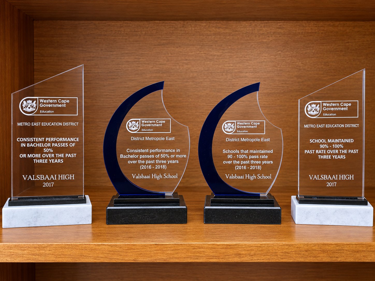 Four Western Cape Education Department trophies on a shelf, awarded to Valsbaai High for consistent Bachelor passes and for maintaining a 90&ndash;100% pass rate